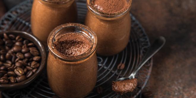 Chocolate mousse in clear glass jars, next to a small dish of coffee beans on a wire metal trivet.