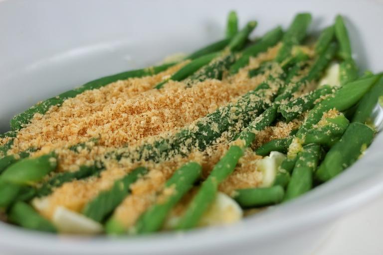 A plate of green beans topped with toasted bread crumbs